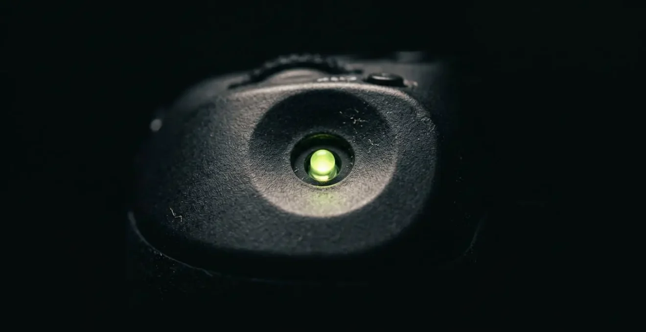 Primer plano de pequeño LED en modo standby emitiendo luz azul en oscuridad total, mostrando contaminación lumínica nocturna